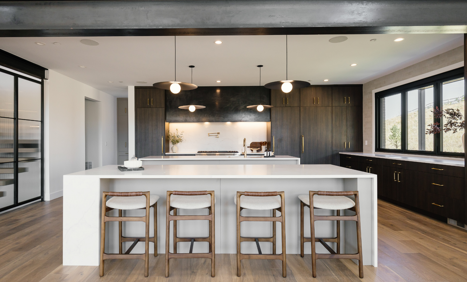 Kitchen with dual waterfall islands, dark wood cabinetry, and hillside views through corner windows in Castle Rock, CO