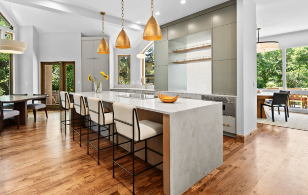 Newly renovated modern kitchen with sage green cabinetry, waterfall quartz island, brass pendant lights, and white oak hardwood floors in Boulder, CO