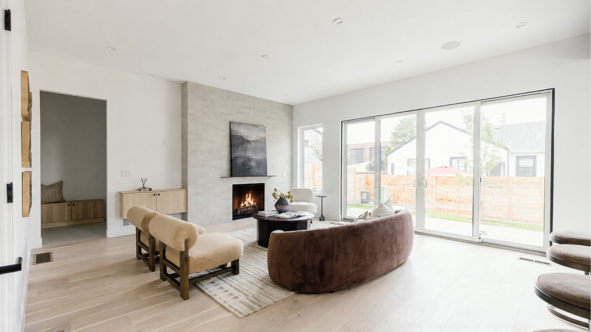 Great room with fireplace, curved sofa, and floor-to-ceiling sliding doors overlooking a fenced backyard