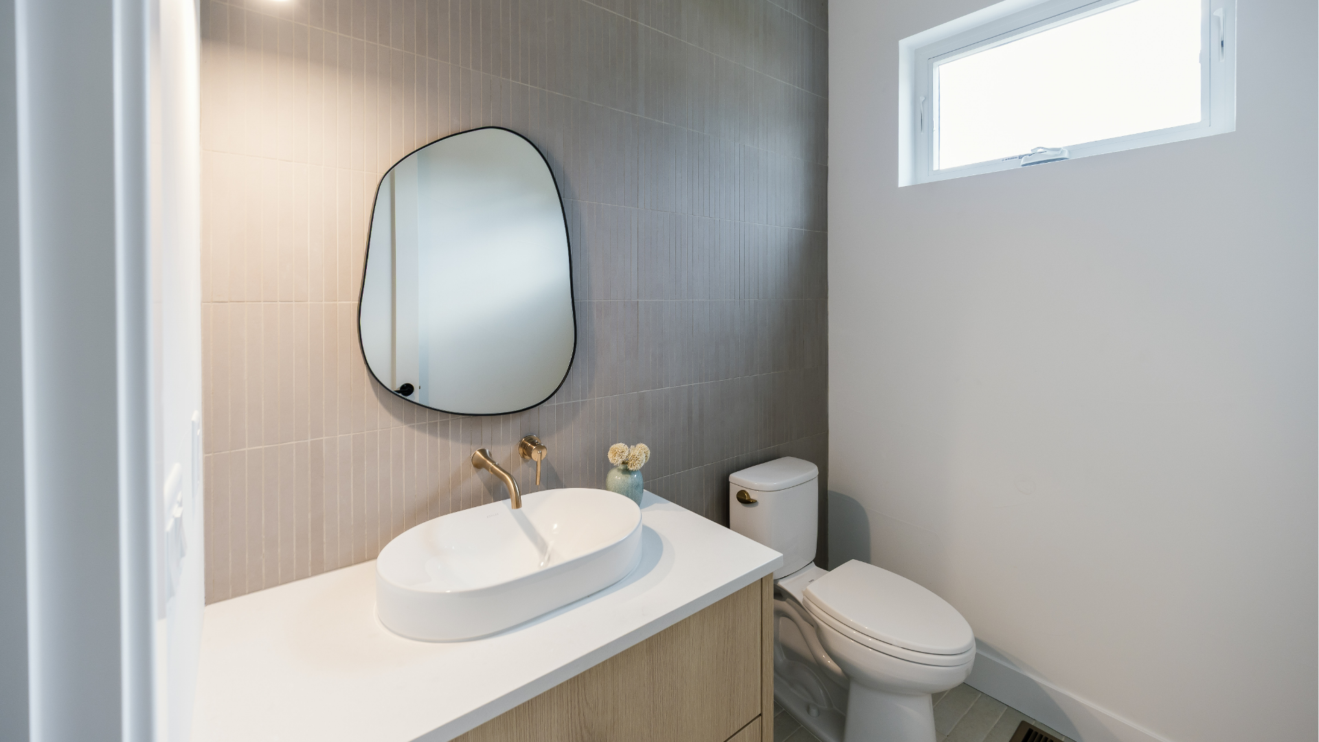 Powder bathroom with organic-shaped mirror, vessel sink, brass fixtures, and textured tile wall