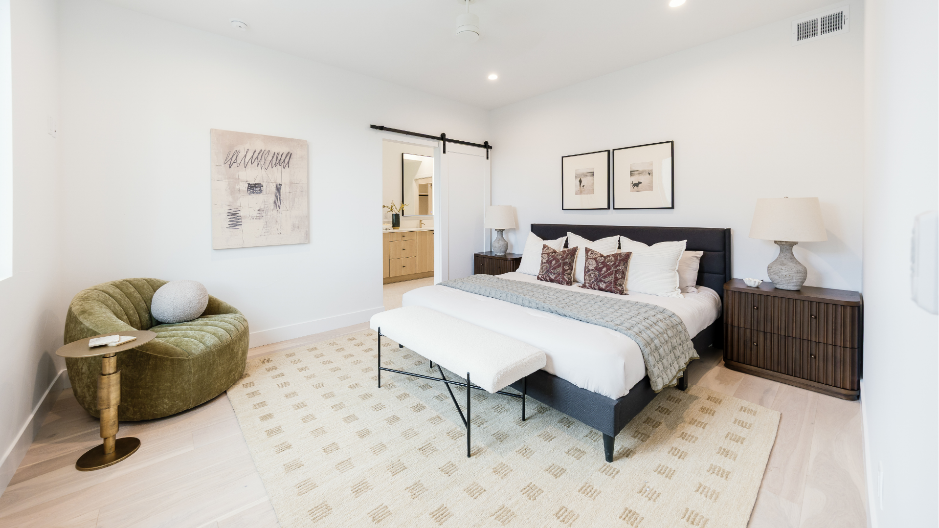Primary bedroom with upholstered bed, olive velvet chair, and barn door leading to the en-suite bathroom