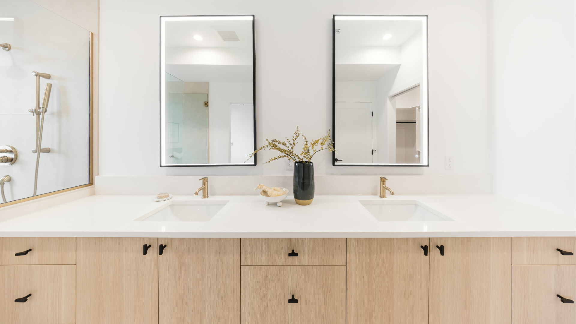 Double vanity with backlit mirrors, brass fixtures, and wood cabinetry