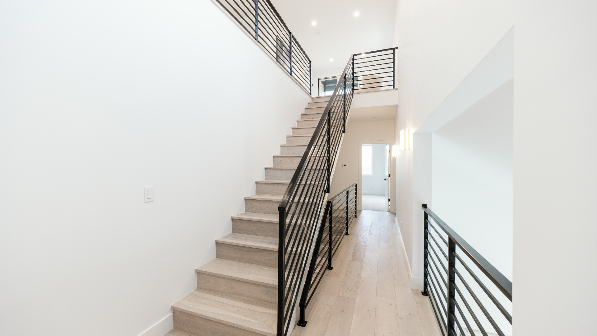 Two-story staircase with black iron railing and hardwood treads leading to an upper-level hallway