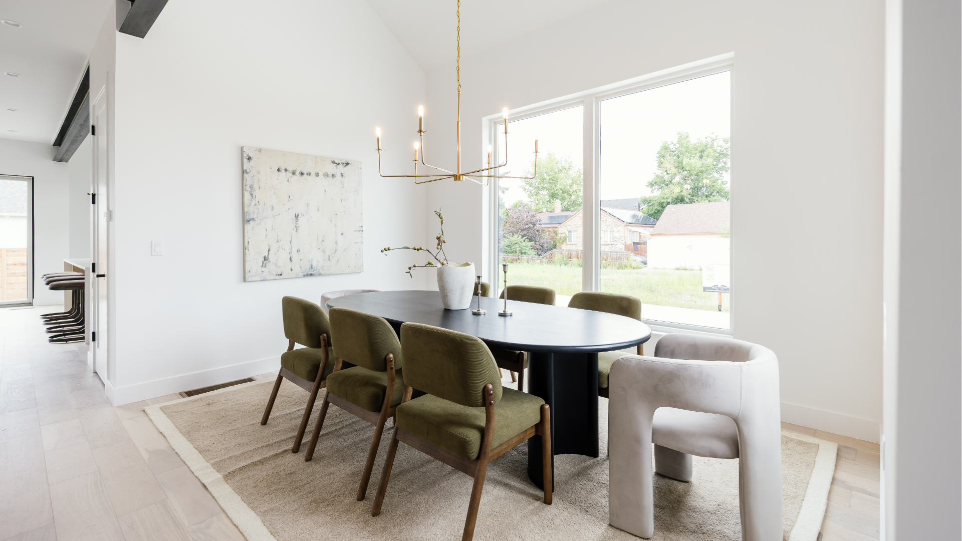Dining room with black oval table, olive green chairs, and brass candelabra chandelier under a vaulted ceiling