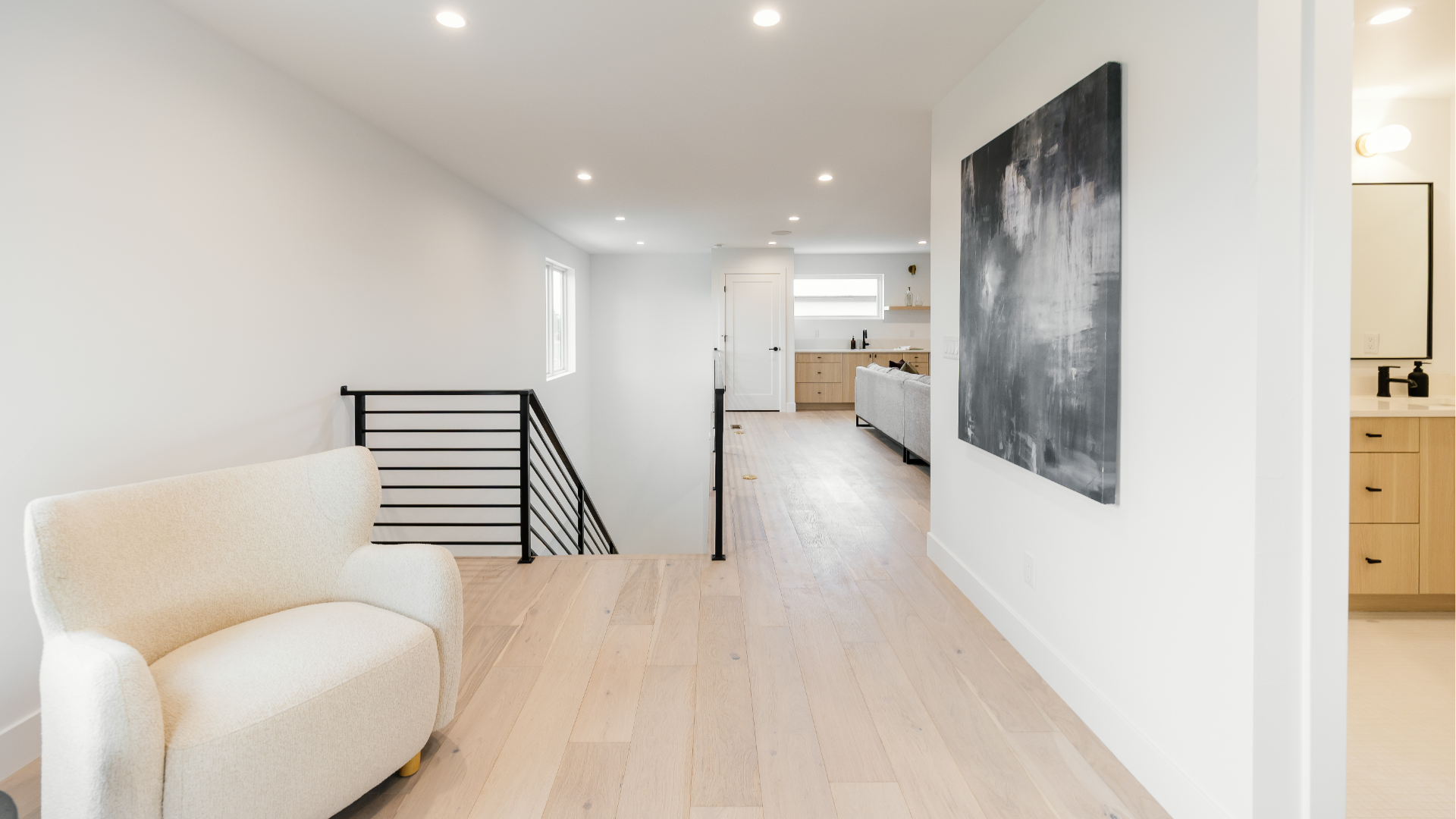 Hallway with black iron stair railing, abstract art, and a view into the third-floor loft living space