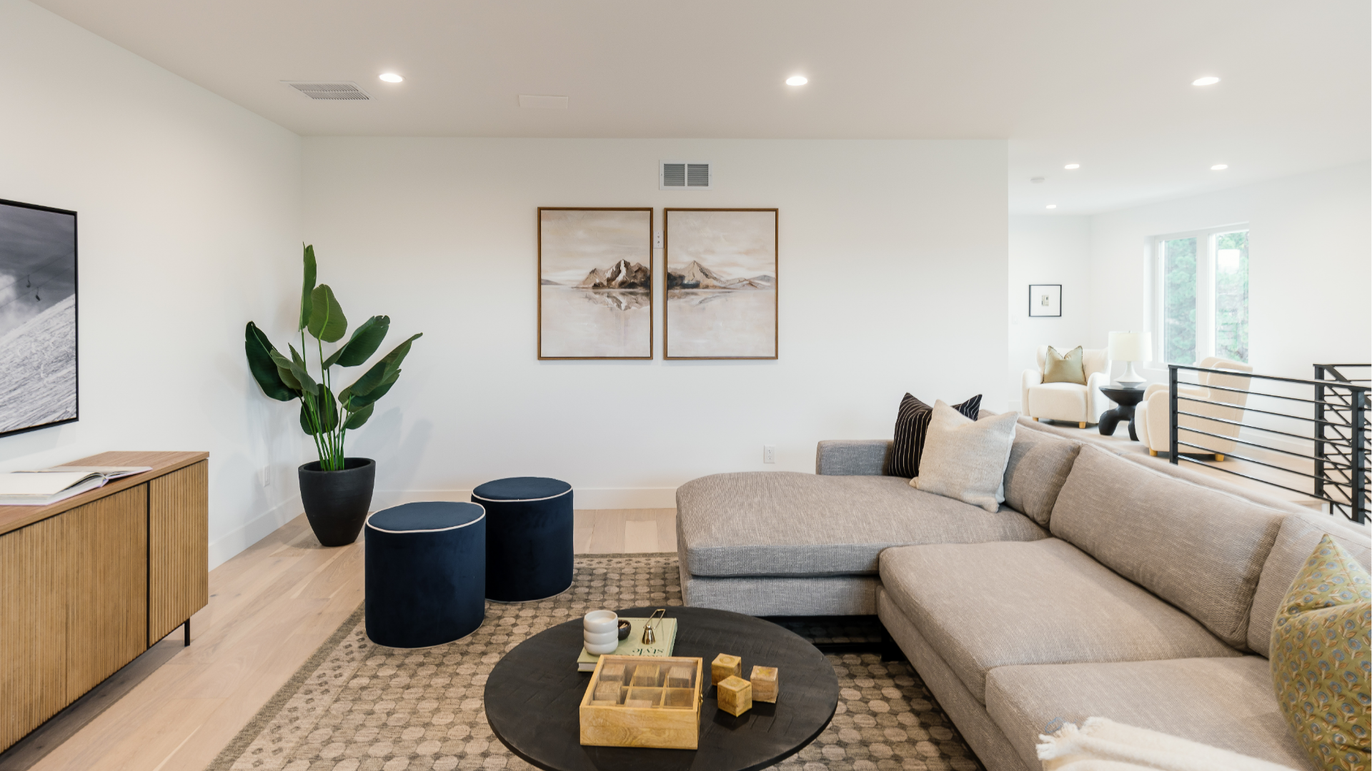 Gray sectional sofa facing a media wall with framed art and a view up to the loft stairs
