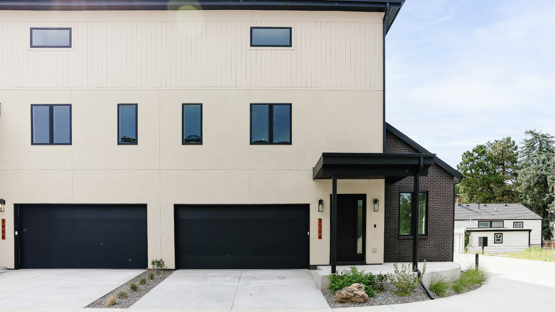 Modern two-story duplex exterior with dark brick, board-and-batten siding, and matching black garage doors