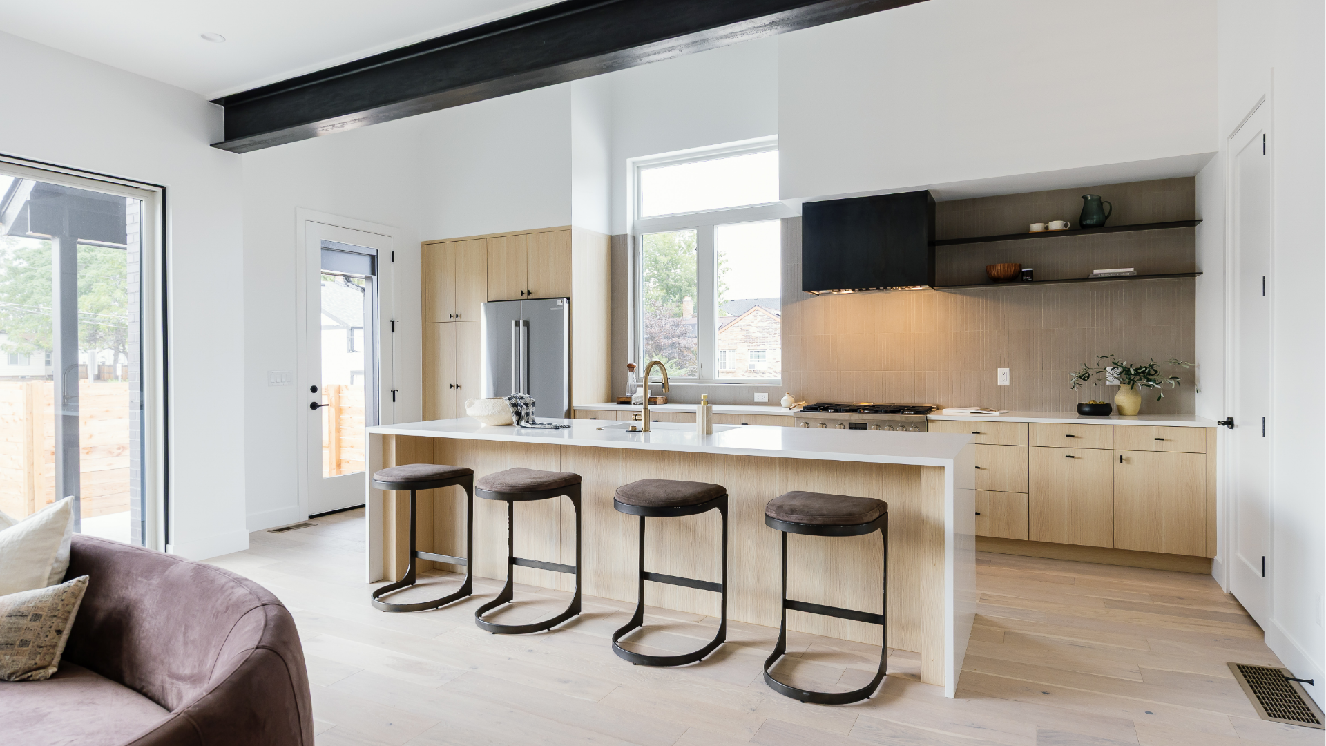 Open kitchen with white waterfall island, wood cabinetry, and custom vent hood viewed from the great room