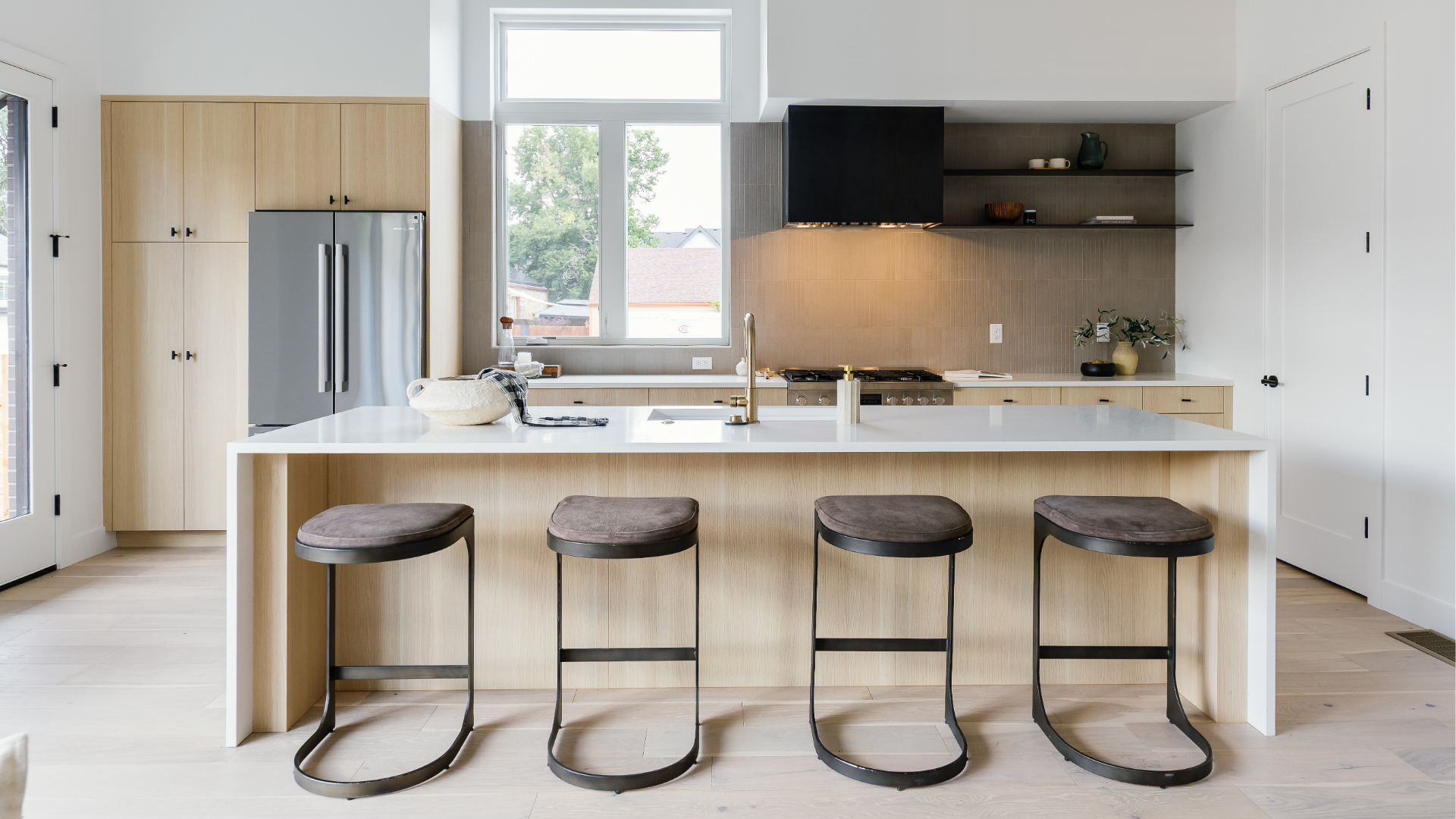 Kitchen island with four counter stools facing a gas range and open shelving