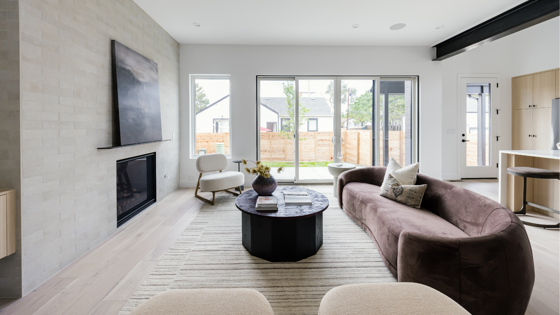 Great room with tile fireplace wall, curved mauve sofa, and wide sliding glass doors to the backyard