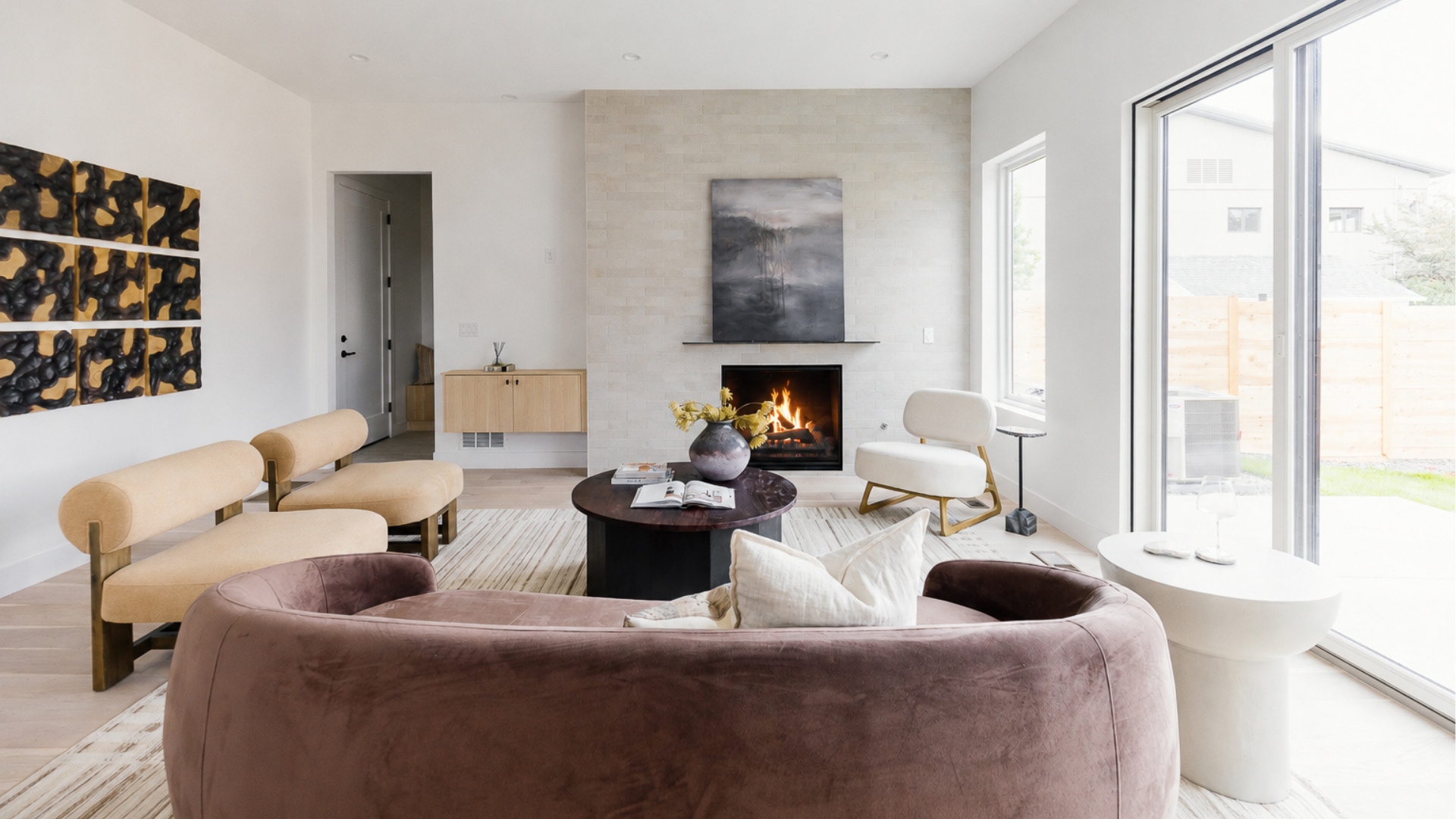 Great room seating arrangement with velvet sofa, cream accent chair, and round coffee table facing a tile fireplace